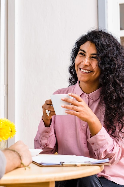 Joven latina sosteniendo una taza de café y sonriendo en un restaurante.