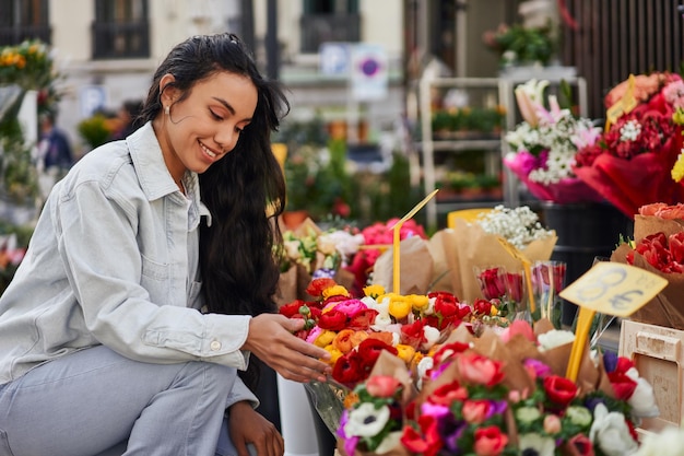 Joven latina vibrante felizmente seleccionando coloridas flores de un vendedor ambulante en una hermosa ciudad