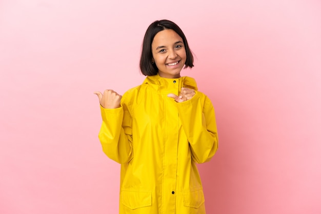 Joven latina vistiendo un abrigo impermeable sobre fondo aislado apuntando hacia el lado para presentar un producto