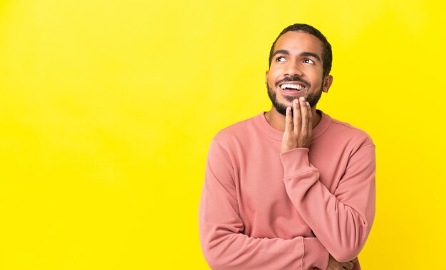 Joven latino aislado de fondo amarillo mirando hacia arriba mientras sonríe