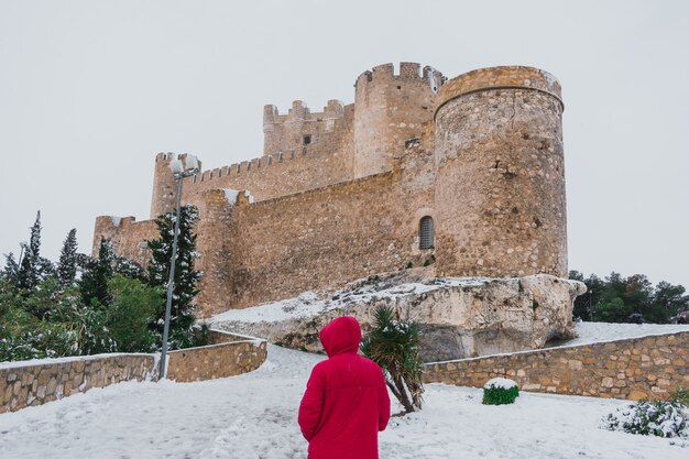 Joven latino camina por un pueblo nevado con un castillo