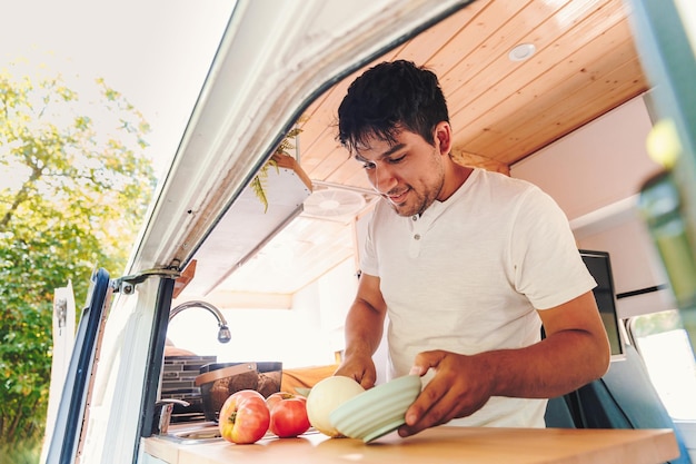 Joven latino cocinando comida en la cocina de su autocaravana hecha a mano Concepto de estilo de vida nómada