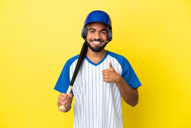 Joven latino colombiano jugando béisbol aislado sobre fondo amarillo dando un pulgar hacia arriba gesto