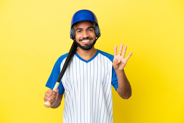 Joven latino colombiano jugando béisbol aislado sobre fondo amarillo feliz y contando cuatro con los dedos