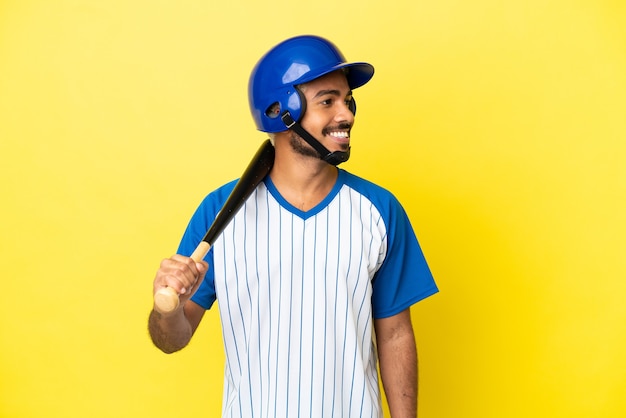 Joven latino colombiano jugando béisbol aislado sobre fondo amarillo mirando hacia el lado