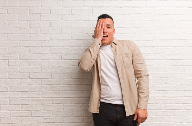 Joven latino gritando feliz y cubriéndose la cara con la mano