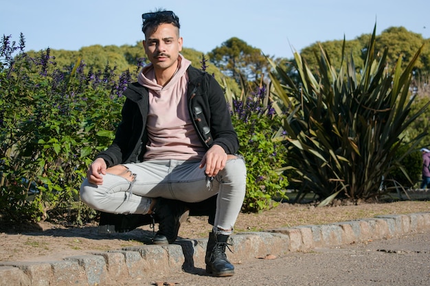 joven latino homosexual agachado posando mirando la cámara en el parque al atardecer estilo de vida