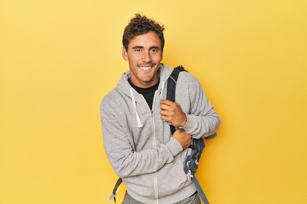 Foto joven latino con mochila de montaña en amarillo riendo y divirtiéndose