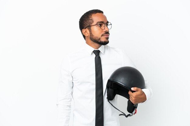 Joven latino de negocios con un casco de motocicleta aislado de fondo blanco mirando hacia un lado