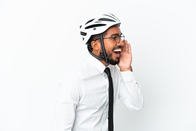 Joven latino de negocios sosteniendo un casco de bicicleta aislado de fondo blanco gritando con la boca abierta al lateral