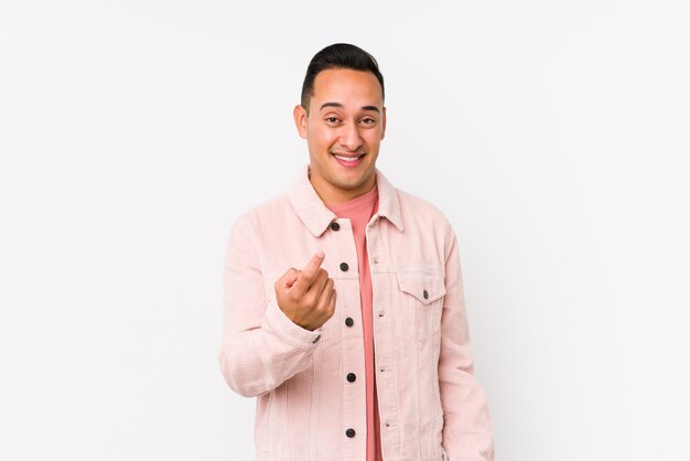 Joven latino posando señalando con el dedo a usted como si invitara a acercarse.