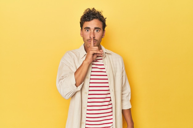 Joven latino posando sobre fondo amarillo guardando un secreto o pidiendo silencio