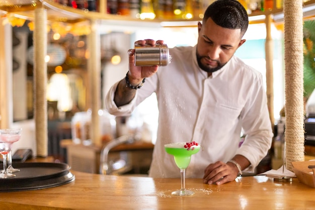 Joven latino preparando cuidadosamente una bebida alcohólica en un moderno bar de cócteles. Espacio para texto. Enfoque selectivo.