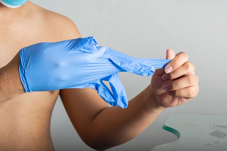 Foto joven latino quitándose los guantes de goma azules después de realizar una operación sanitaria sin camisa