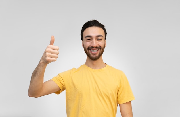 Joven latino sonriendo a la cámara con los pulgares hacia arriba en el fondo blanco