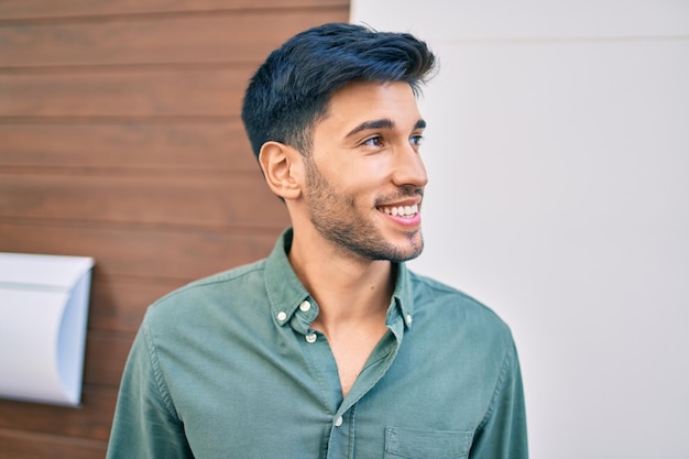 Joven latino sonriendo feliz caminando por la ciudad.