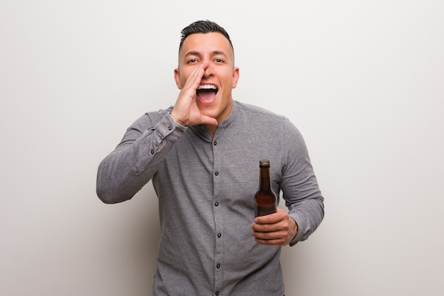 Joven latino sosteniendo una cerveza gritando algo feliz al frente