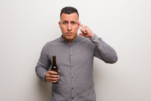 Joven latino sosteniendo una cerveza pensando en una idea
