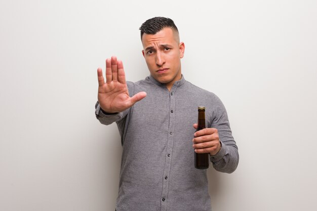 Foto joven latino sosteniendo una cerveza poniendo la mano delante