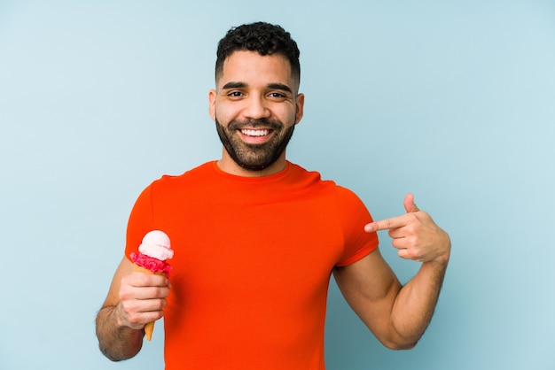 Joven latino sosteniendo una persona aislada de helado apuntando con la mano a un espacio de copia de camisa, orgulloso y seguro