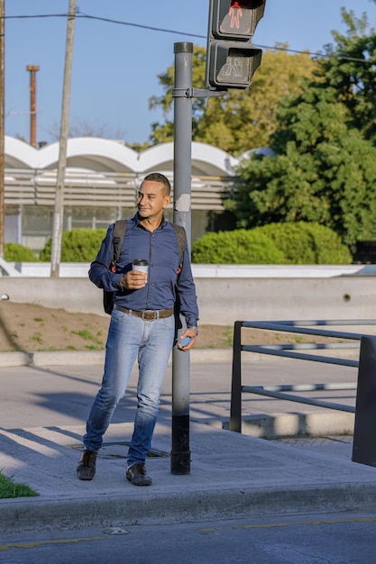 Foto joven latino con una taza de café de papel en la mano espera cruzar la calle en una ciudad