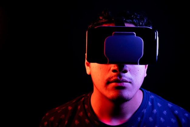 Joven latino usando Realidad Virtual Auriculares VR Gafas 3D Fondo oscuro Espacio de copia de clave baja