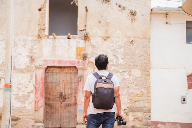 joven latino viajando fotógrafo con la espalda girada explorando la ciudad antigua con la cámara