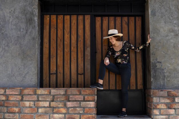 Joven latinoamericana 22 con poses de sombrero de vaquero de pie frente a la entrada de fondo de madera Espacio de copia Concepto de modelo