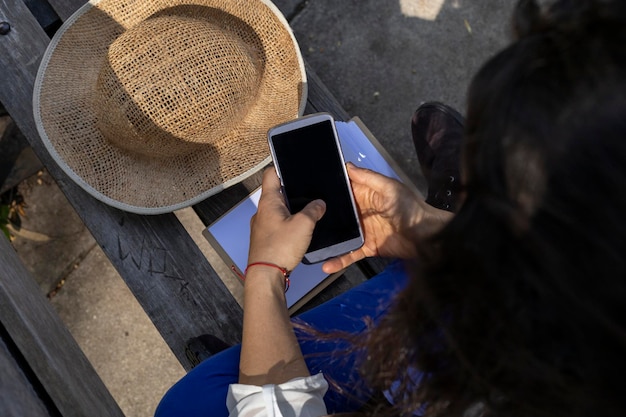 Joven latinoamericana 33 irreconocible aprovecha la llegada de la primavera para sentarse en un banco del parque y escribir mensajes de texto en su celular Concepto de primavera