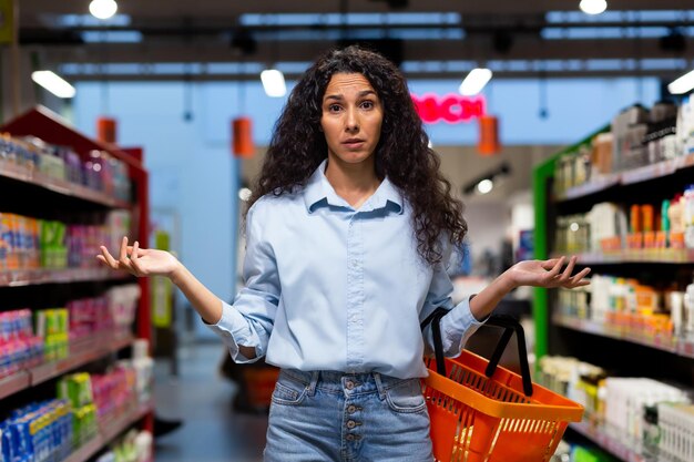 Una joven latinoamericana preocupada se encuentra en un supermercado entre los estantes con productos que sostienen un