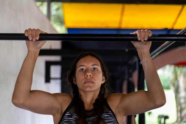Joven latinoamericana prueba la fuerza de su brazo en la barra de calistenia durante su entrenamiento en el gimnasio Concepto de estilo de vida saludable