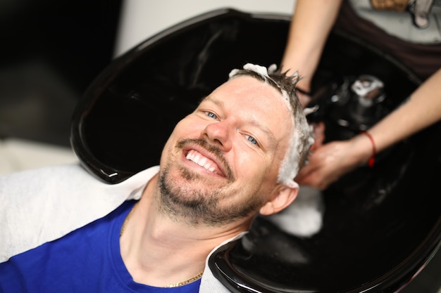 Joven lava el cabello con champú en el lavabo en el salón de belleza