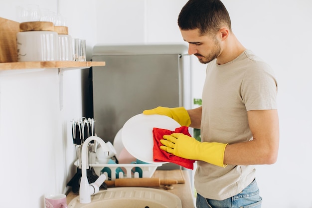 Un joven lava platos en la cocina limpia un plato