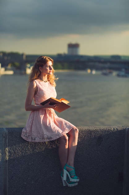 Una joven leyendo un libro en la orilla del río.