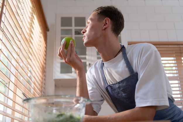 Joven LGBT entra en la cocina para hacer una ensalada de frutas y verduras para la cena Comiendo manzana