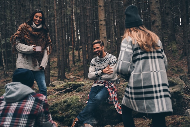 Joven y libre. Grupo de jóvenes felices de pie alrededor de la fogata mientras camina en el bosque