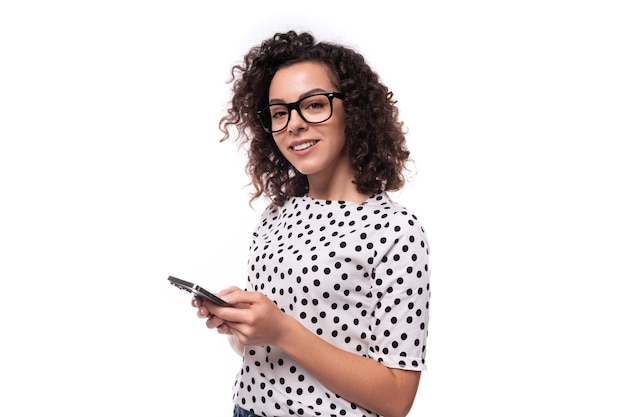 Foto una joven líder con el peinado rizado vestida con una blusa de verano escribe un mensaje en su teléfono inteligente