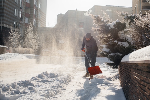 Un joven limpia la nieve frente a la casa en un día soleado y helado. Limpiar la calle de la nieve.
