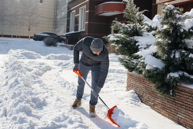 Un joven limpia la nieve frente a la casa en un día soleado y helado. Limpiar la calle de la nieve.