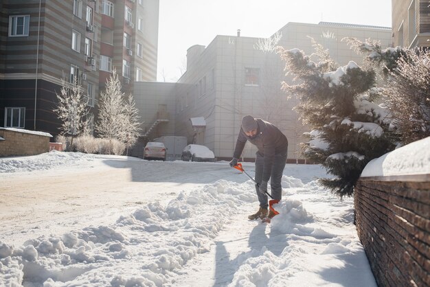 Un joven limpia la nieve frente a la casa en un día soleado y helado. Limpiar la calle de la nieve.