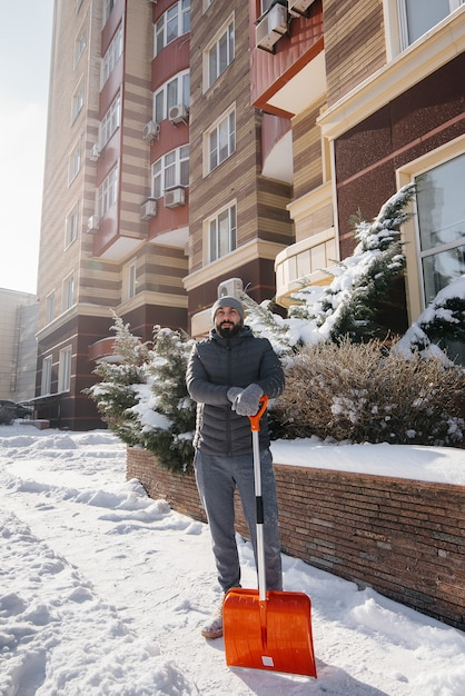 Un joven limpia la nieve frente a la casa en un día soleado y helado.