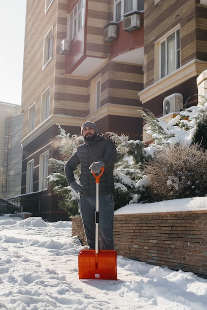 Un joven limpia la nieve frente a la casa en un día soleado y helado.