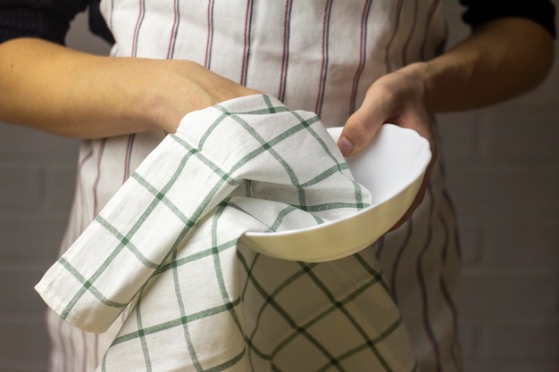 Un joven limpia un plato con una toalla de algodón.