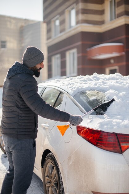 Un joven limpia su automóvil después de una nevada en un día soleado y helado.