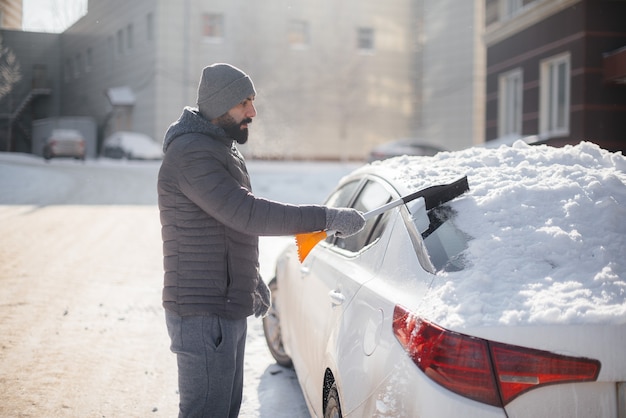 Un joven limpia su automóvil después de una nevada en un día soleado y helado.