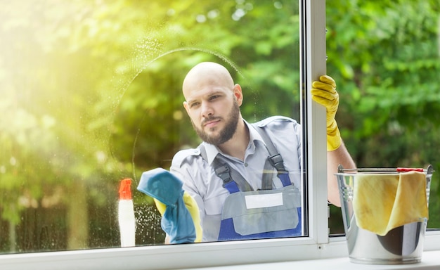 Joven limpiador lavando ventana en el día al aire libre