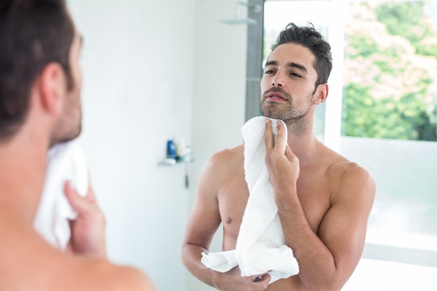 Foto joven limpiando la cara mientras se mira en el espejo