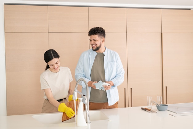 Joven limpiando platos limpios lavados por su esposa en la cocina