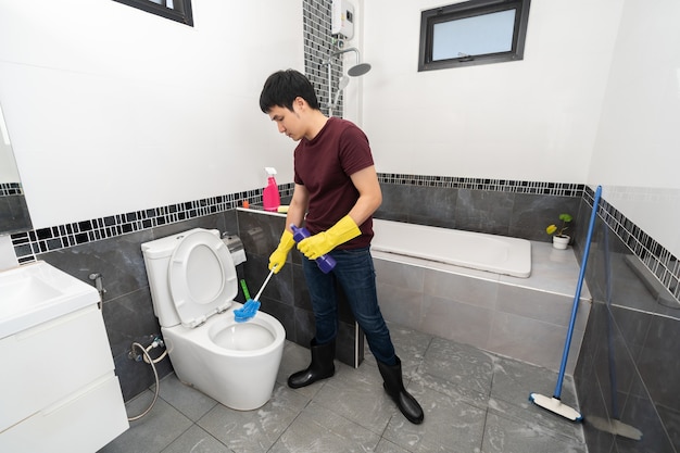 Joven limpieza de la taza del inodoro en el baño.