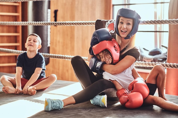 Una joven linda con casco y su hermosa entrenadora de boxeo están posando para el fotógrafo en el ring.